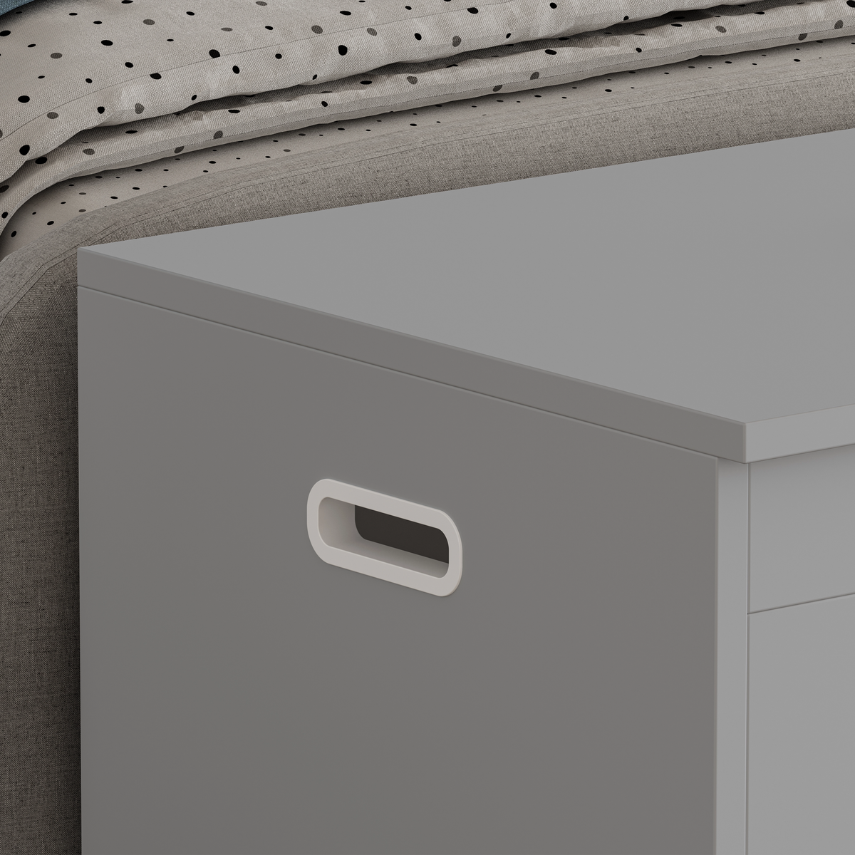 Gray storage bin with a handle next to a bed with polka dot bedding.