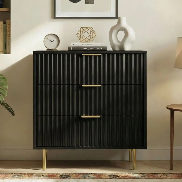 [Black] Three drawer black chest of drawers with flutrina detailing and gold legs in a natural light room setting