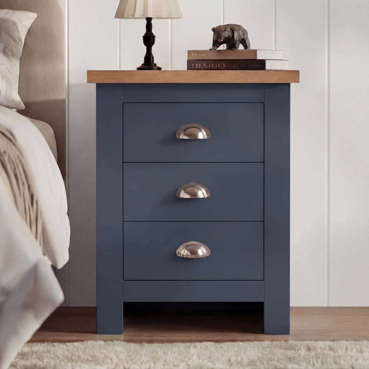 [Blue] Front view of 3 drawer shaker bedside table with oak top and cup handles styled beside bed with lamp