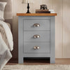 [Grey] 3 drawer nightstand with shaker styling and oak top surface displaying lamp and decorative items