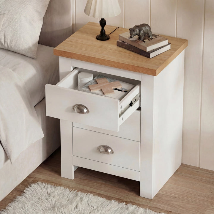 [White] Top drawer of white shaker bedside open with folded fabric items inside, lamp and bear on oak top