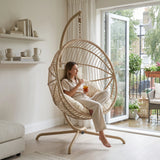 [Beige] Woman sitting in a hanging rattan chair in a bright living room