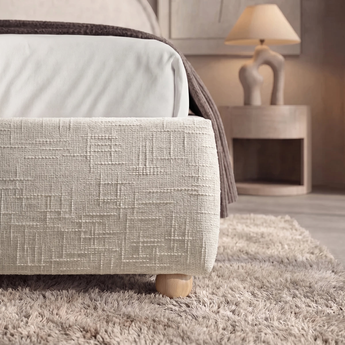 [Double | Beige] Embracea footboard close-up highlighting woven textured fabric and natural rounded wooden legs on shaggy rug