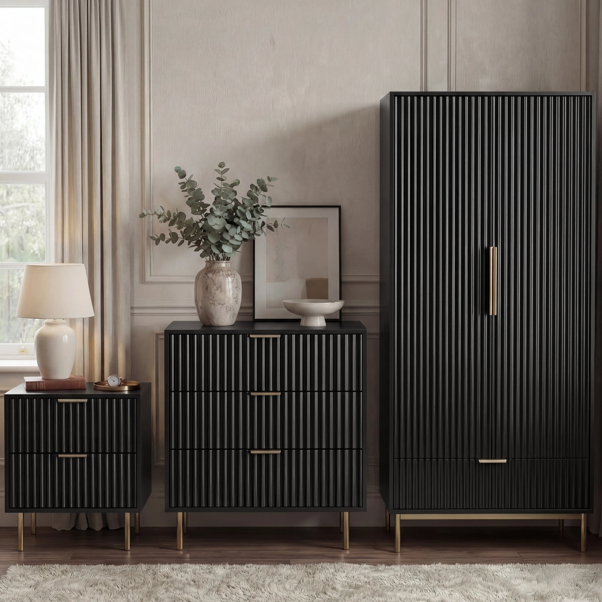 [Black] flutrina black 2 door wardrobe, 3 drawer chest and 2 drawer bedside grouped on brass legs against a panelled wall