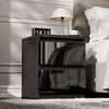 [Black] bedside table with a clock and cup next to a bed in a bedroom setting