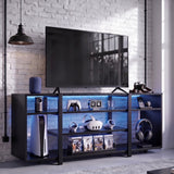 [Black Carbon Fibre] LED TV Stand with Storage styled in a gaming room with blue LED shelf lighting, open shelves holding a console, VR headset and game cases