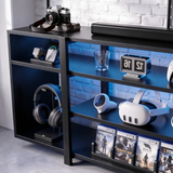 [Black Carbon Fibre] Zelumi TV stand right-side close-up showing blue LED-lit shelves with headset, VR gear, clock, charger and game cases displayed