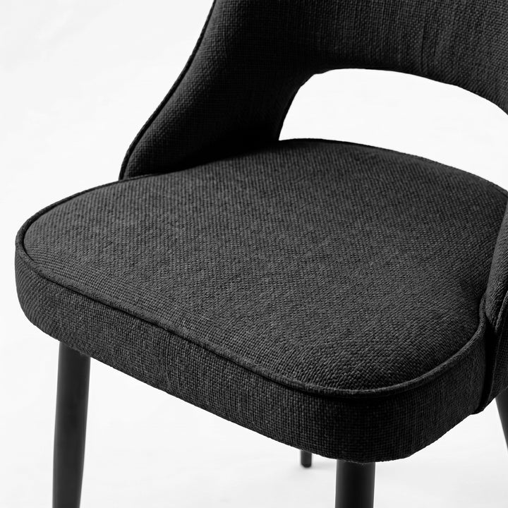 [Black | Set of 4] Comfy dining chair close-up of padded seat, piped edge, curved open back and black metal legs.