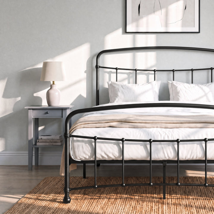 [Black | Double] Close view of the black curved front rail, vertical bars and white bedding beside a small table.