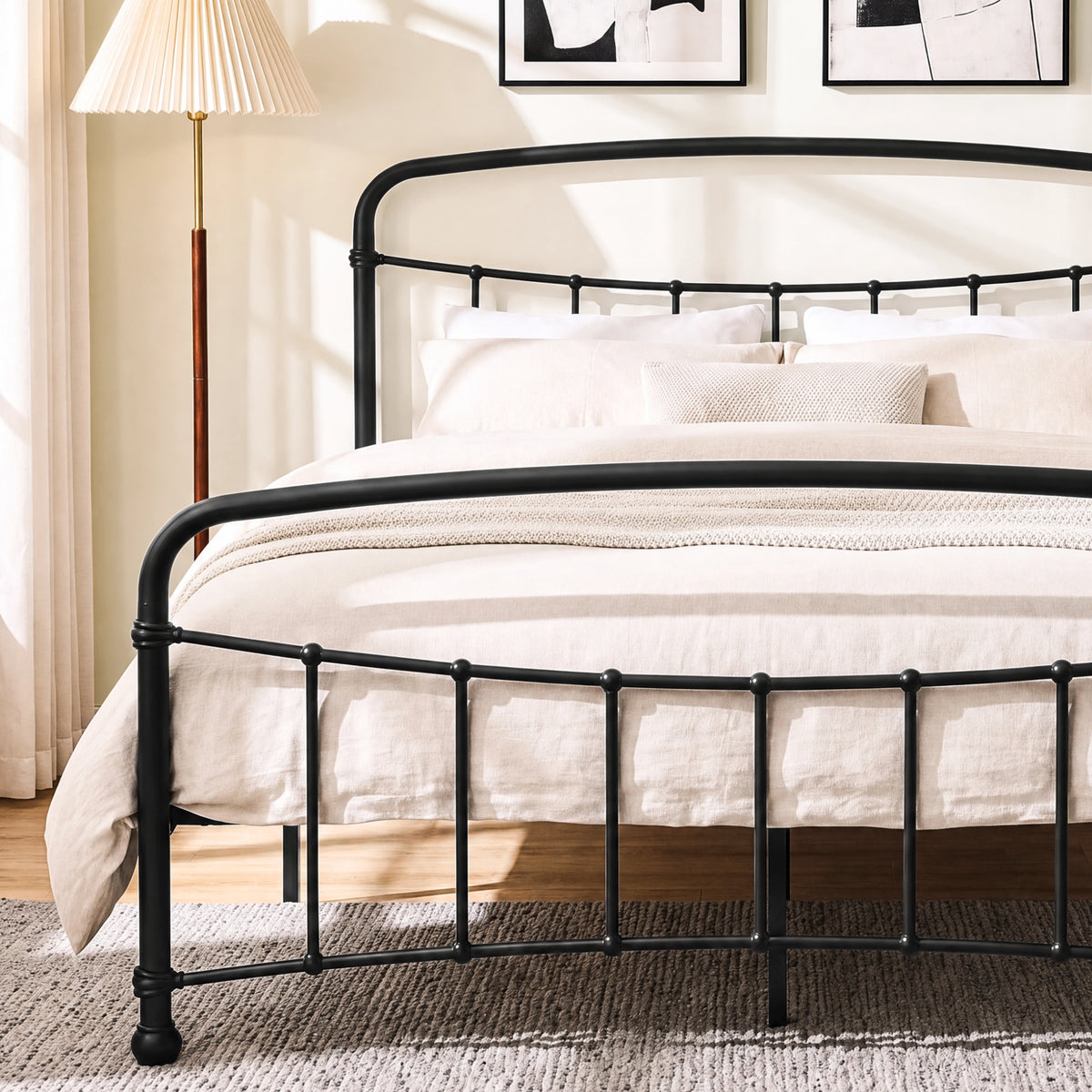 [Black | King] Close view of the black curved front rail, vertical bars and cream bedding beside a lamp.