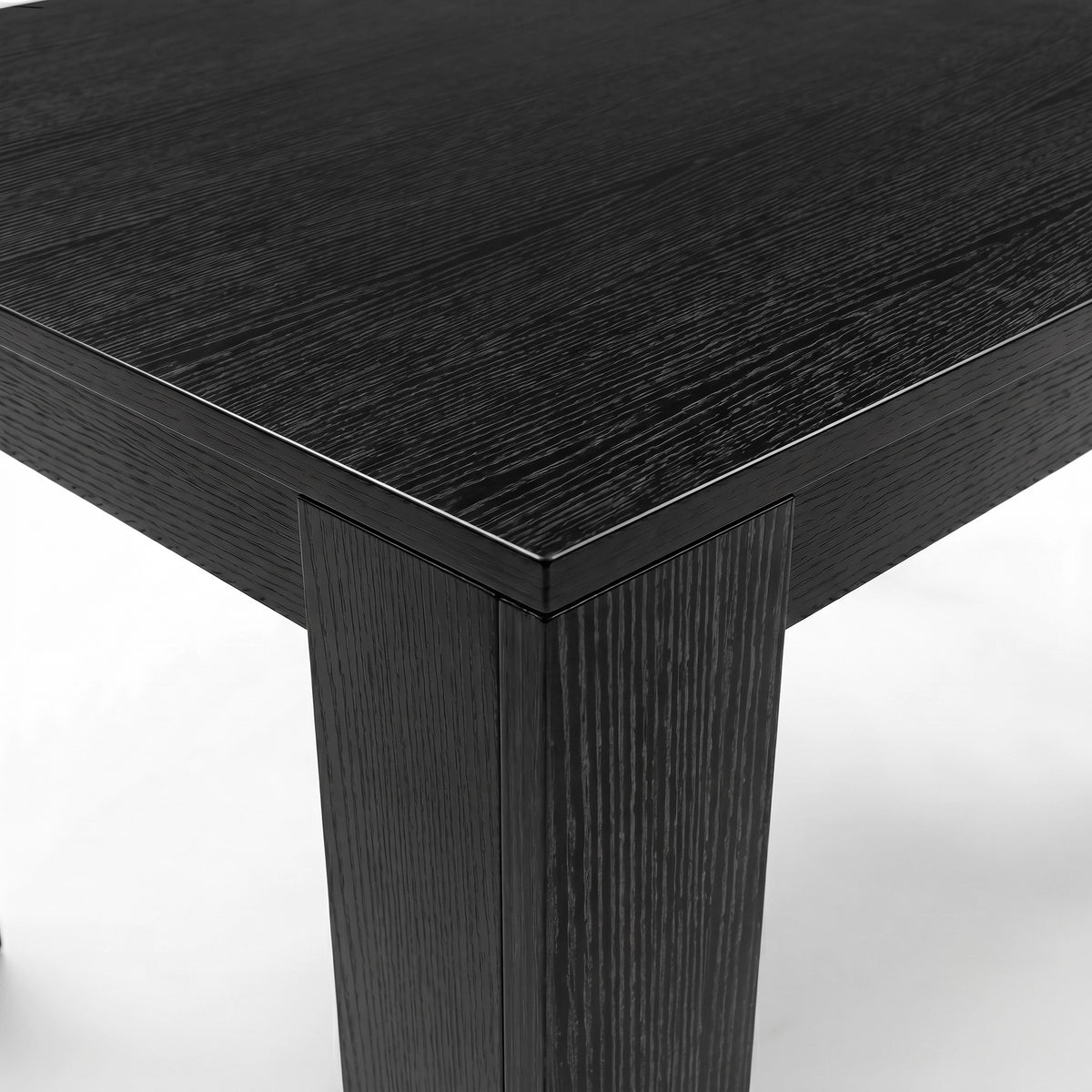 [Black Wood] Close-up of the black wood-effect tabletop corner and thick L-shaped leg; fine grain runs across the surface.