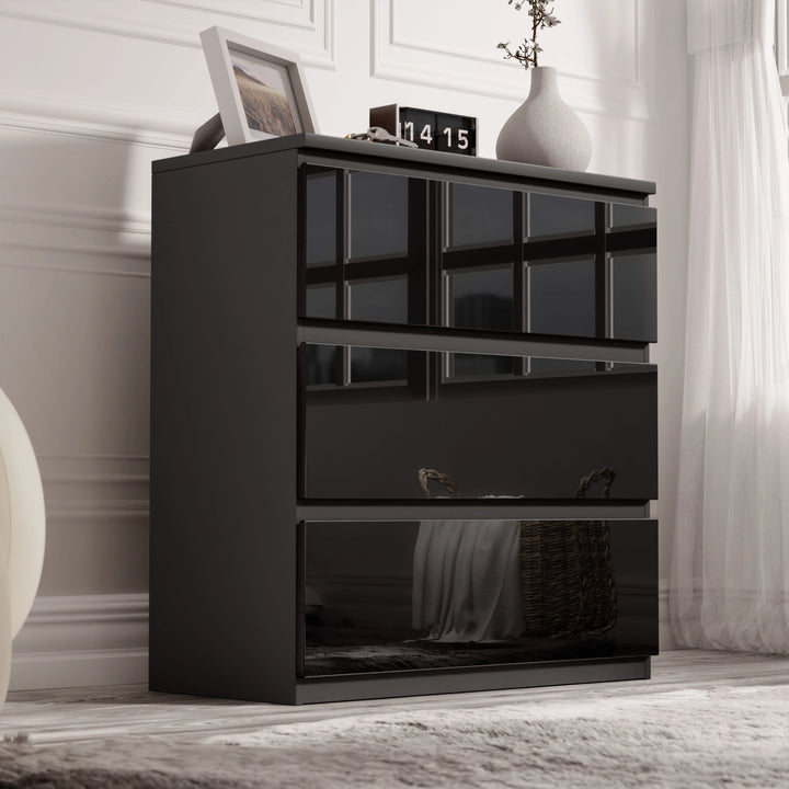 [Black] high gloss 3 drawer chest styled against white panelled wall with vases and clock