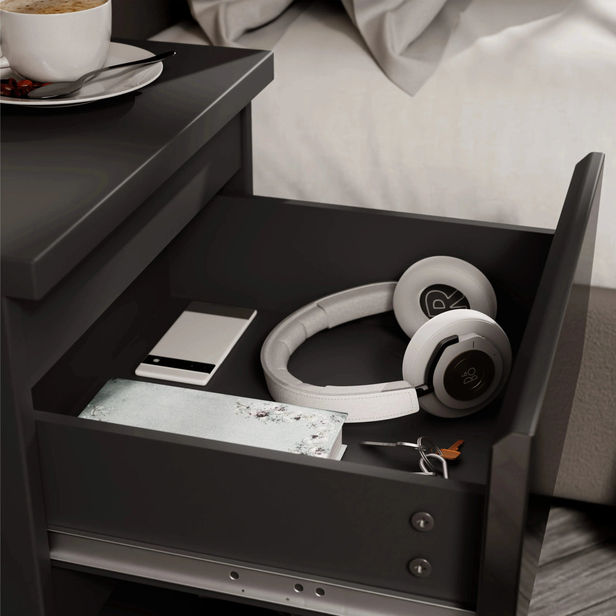 [Black] close-up of open drawer in black bedside table showing phone headphones notebook and keys