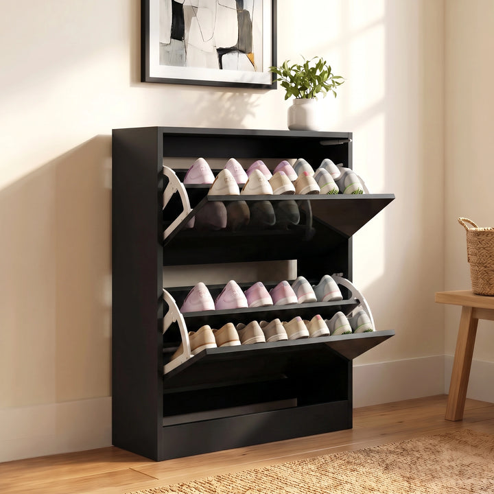 [Black] shoe rack with two tier holding several pairs of shoes, shown in a styled room setting with a wall frame, small plant, and woven basket.