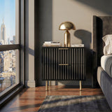 [Black] bedside cabinet with flutrina detailing and gold legs positioned beside a bed for storage