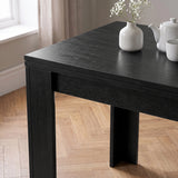 [Black] Close-up of folded wood-grain tabletop above apron and wide legs, with flower vase, teapot and cup