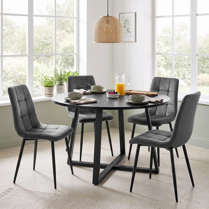 [Black Wood] Round dining table set for four in a bright breakfast room with grey chairs surrounding the cross-leg base.