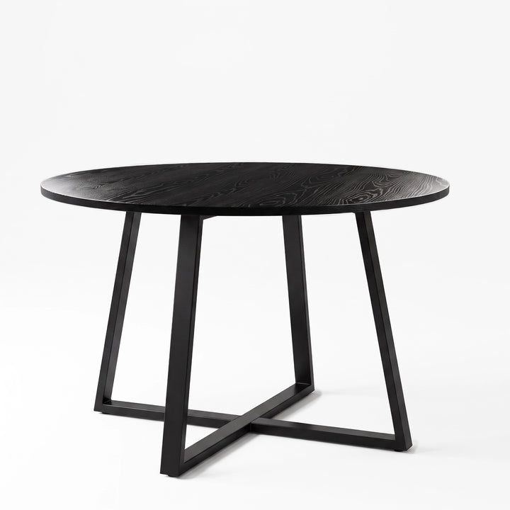 [Black Wood] Round wood-effect dining table in a studio view with the tabletop resting above a black iron cross base.