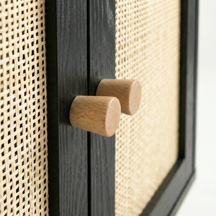 [Black] Wovena close-up of two solid cylindrical oak knob handles on the ebonised centre door divider, with open-weave rattan panels filling the frame on both sides