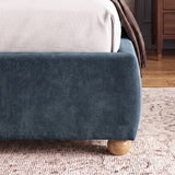 [Double | Blue] Lower corner of a blue fabric bed frame with rounded edges and small wooden legs placed on wooden flooring