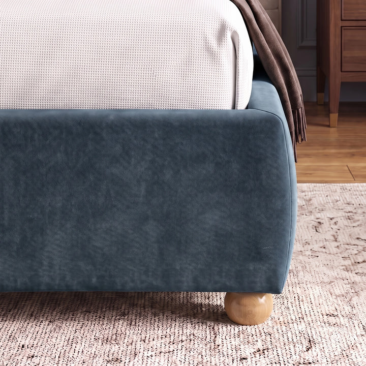 [Double | Blue] Lower corner of a blue fabric bed frame with rounded edges and small wooden legs placed on wooden flooring