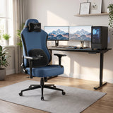 [Blue] ergonomic gaming office chair with black accents and a headrest pillow, positioned in front of a black computer desk setup with dual monitors in a bright home office