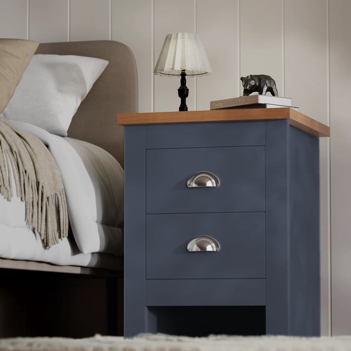 [Blue] side view blue 2 drawer bedside table with cream throw on adjacent bed and panelled wall
