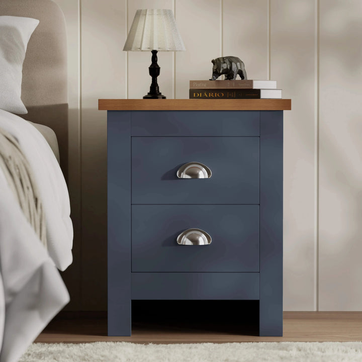 [Blue] bedside table with lamp and books on oak top next to upholstered headboard