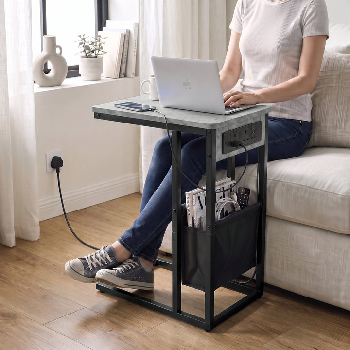 [Concrete] C-shaped side table used for laptop work by sofa with charging station plugged in wall socket and storage pouch