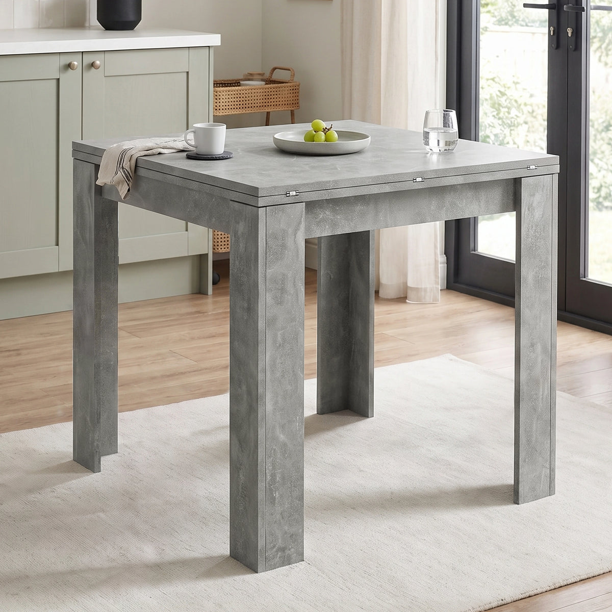 [Concrete] Closed square flip-top dining table styled with a mug, fruit bowl and glass in a bright kitchen