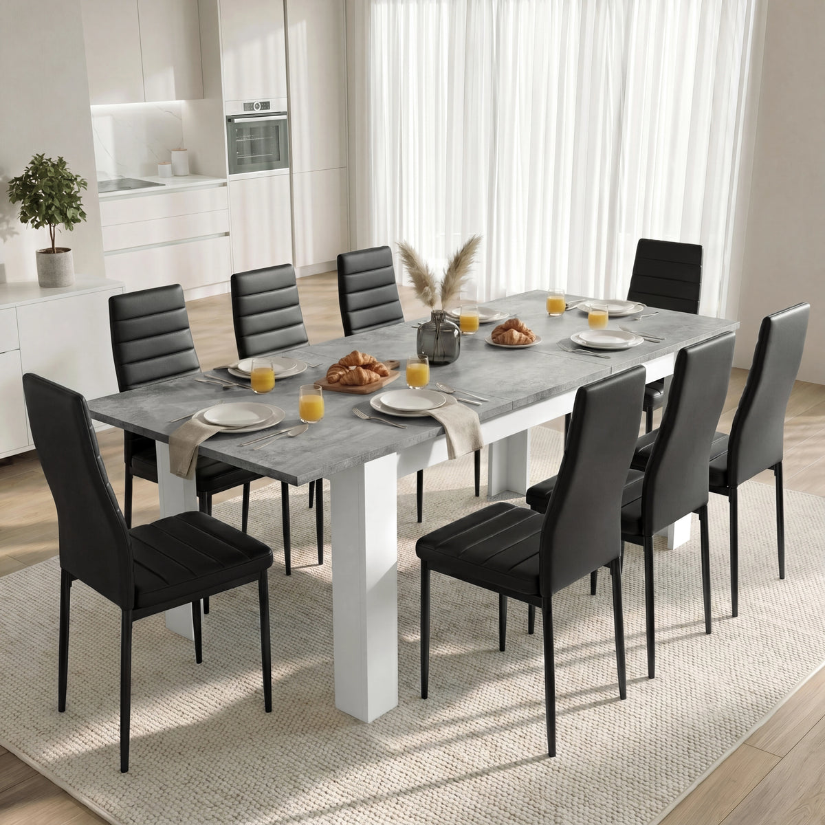 [Concrete] Extended concrete-effect dining table for 6-8 at breakfast; 8 black chairs surround its thick white legs.