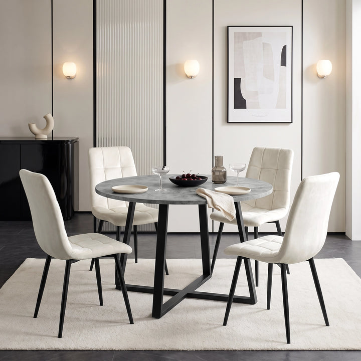 [Concrete] Round dining table set for four with plates and glasses, surrounded by white chairs on a neutral rug.