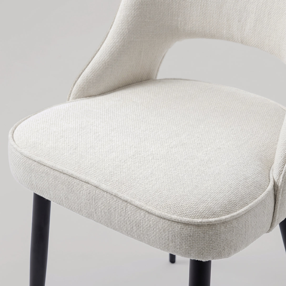 [Cream | Set of 4] Comfy dining chair close-up view of woven seat, piped edge, curved open back & black metal legs.