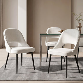 [Cream | Set of 4] Four upholstered comfy dining chairs styled around a glass table with chrome legs, fruit bowl and vase.