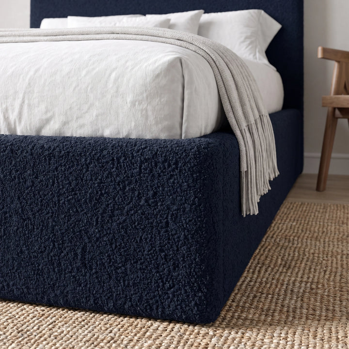 [Double | Blue] Three-quarter view of curved headboard and bedding showing boucle texture with fringed throw draped across