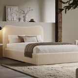 [Double | Beige] Boucle fabric ottoman bed from the side with white bedding and fringed throw beside floating shelf with art