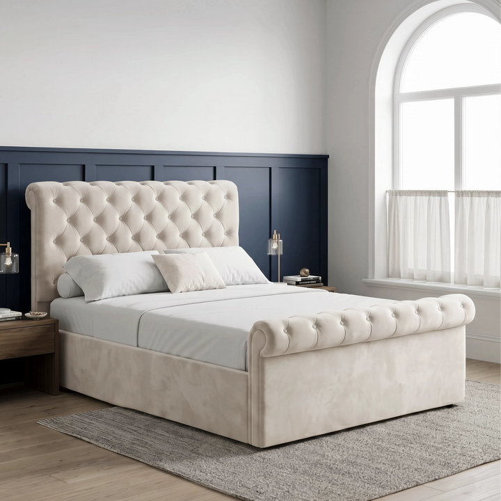 [Double | Beige] Angled bedroom view with tufted headboard, rolled footboard, glass lamps, blue panels, and arched window