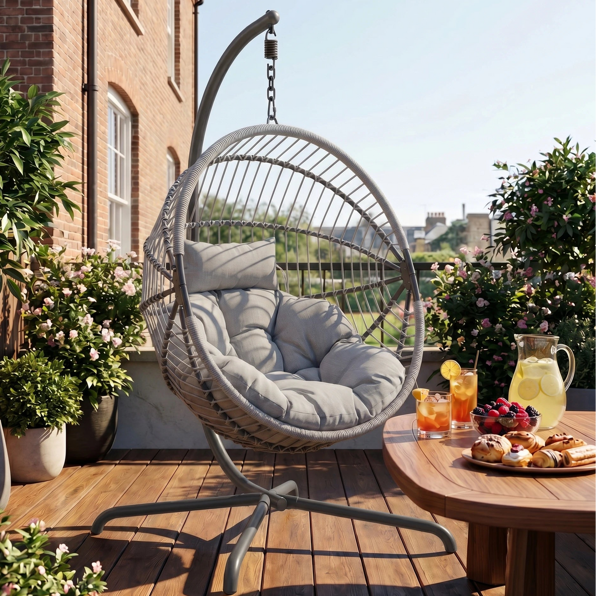 [Grey] Hanging chair on a wooden deck with a table of snacks and drinks, surrounded by plants and a building in the background