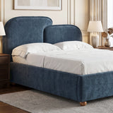 [Double | Blue] upholstered bed frame with a tall curved headboard and matching footboard, shown in a styled bedroom setting with white bedding, bedside tables, lamps, and a rug.
