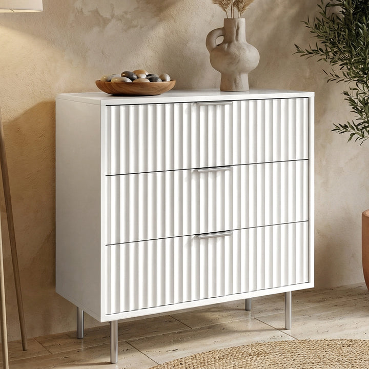 [White] painted three drawer chest from the right with vertical fluted fronts and silver cylindrical legs