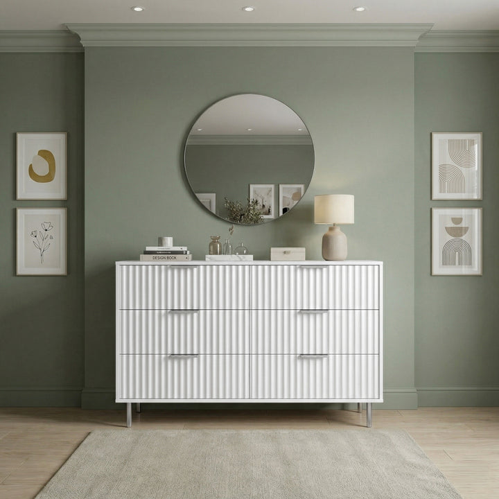[White] chest of drawers with decorative items against a green wall placed in a natural light room front view