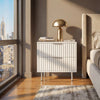 [White] flutrina two drawer bedside table with metal handles placed beside a bed in a softly lit bedroom