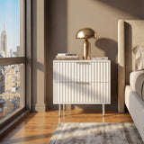 [White] flutrina two drawer bedside table with metal handles placed beside a bed in a softly lit bedroom