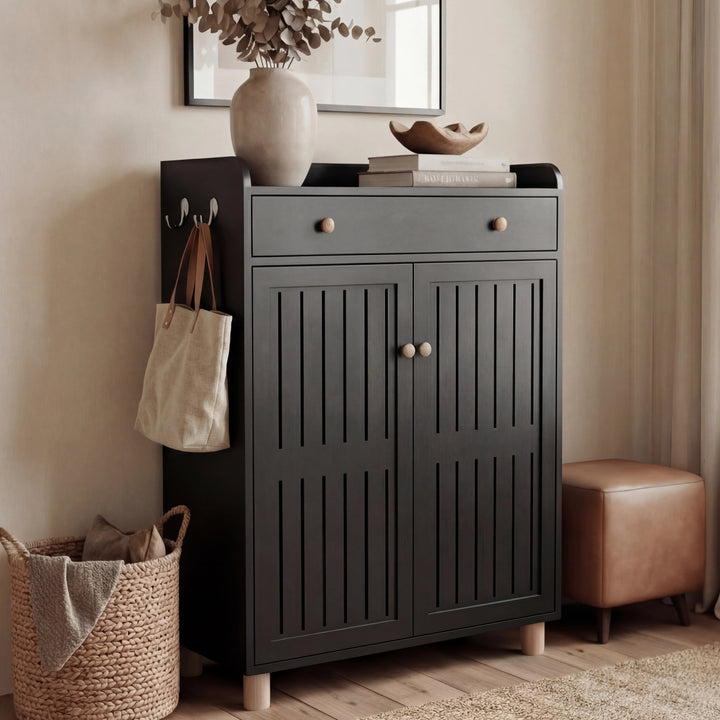 [Black] Closed-door black shoe storage cabinet beside a woven basket and pouf, top holds a vase and decorative bowl