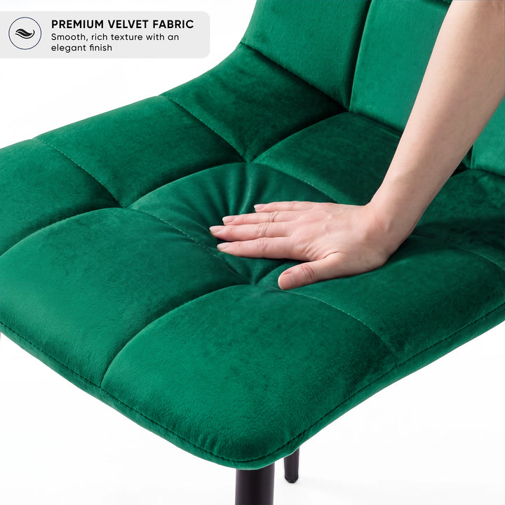 [Green] Velvet dining chair cushion close-up, with a hand pressing into the tufted seat beside its curved edge.