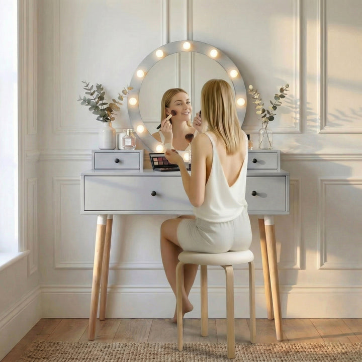 [Grey] Dressing Table With Drawers lifestyle scene with a woman applying makeup at the lit Hollywood mirror beside eucalyptus and perfume bottles