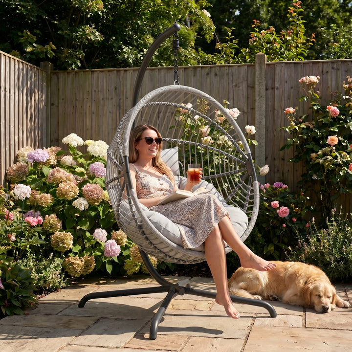 [Grey] Woman relaxing in a hanging chair with a dog in a garden setting