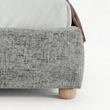[King | Grey] Embracea bed base close-up showing curved footboard profile, woven fabric texture, and solid oak round leg