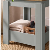 [Grey] Close-up of the square side table's open lower storage holding a folded throw and basket of remote controls