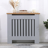 [Small | Grey] Radiator Cover with oak top shelf styled with dried grass, stacked books, and a candle against a bright white wall